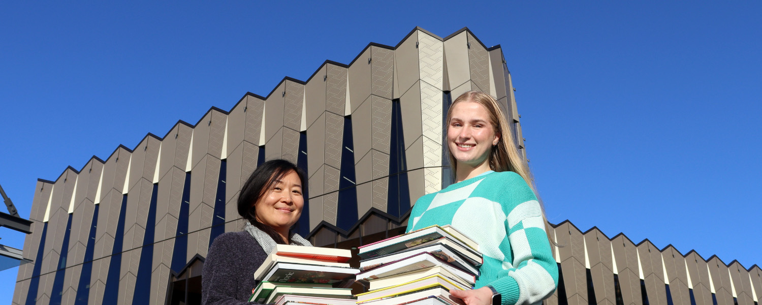 Library visitors holding books outside Tauranga Library.